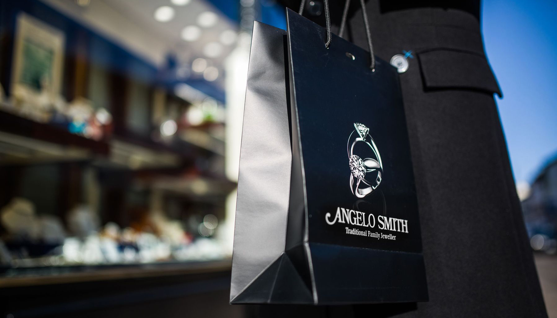 An Angelo Smith branded carrier bag is held outside the showroom window.