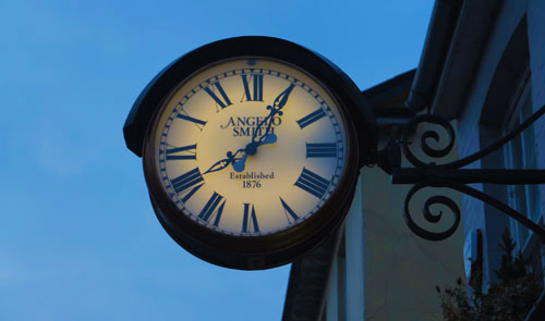 A large clock hangs on the side of a building, against a blue sky.